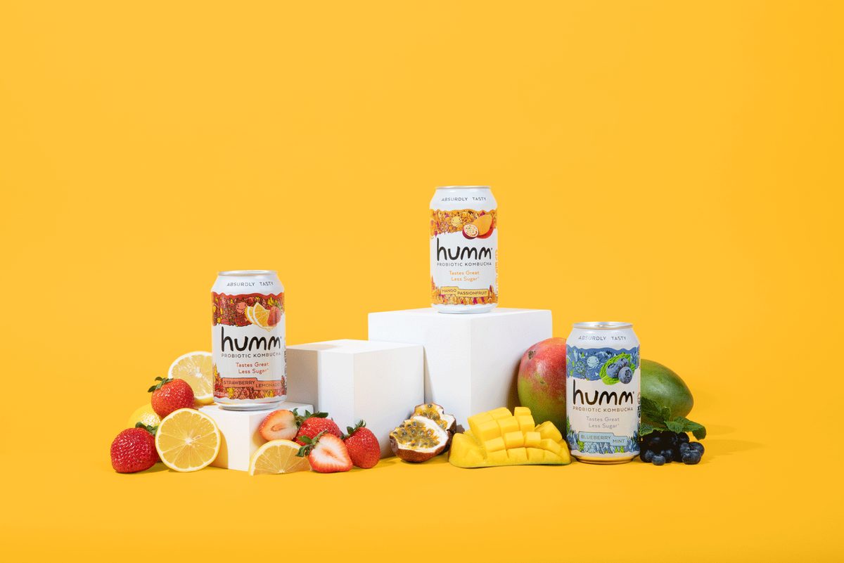 Kombucha poured over ice, with the flavour range and fresh fruit on a yellow field